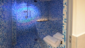 A bathroom with mosaic tile walls and floor, a shower area, and a towel rack with towels. - Barbarella Suite (Naples)