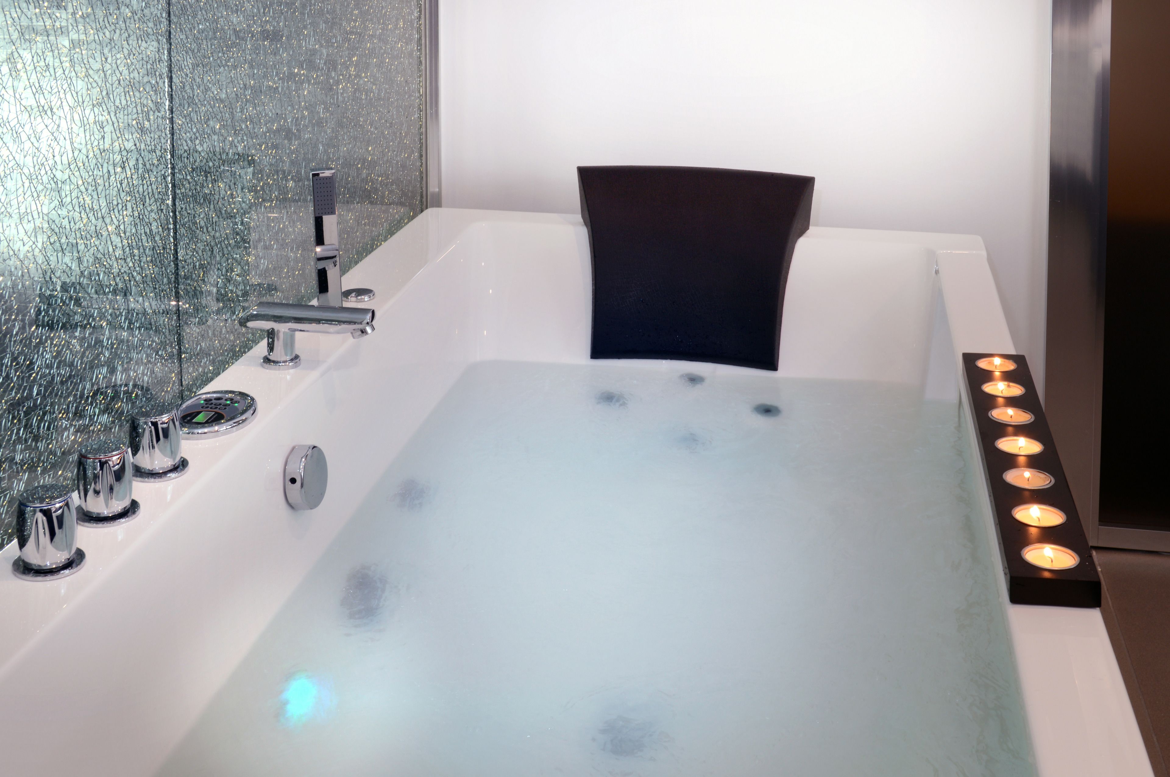 Une salle de bain moderne avec une baignoire entourée de parois en verre, des robinetteries chromées et une rangée de bougies allumées.