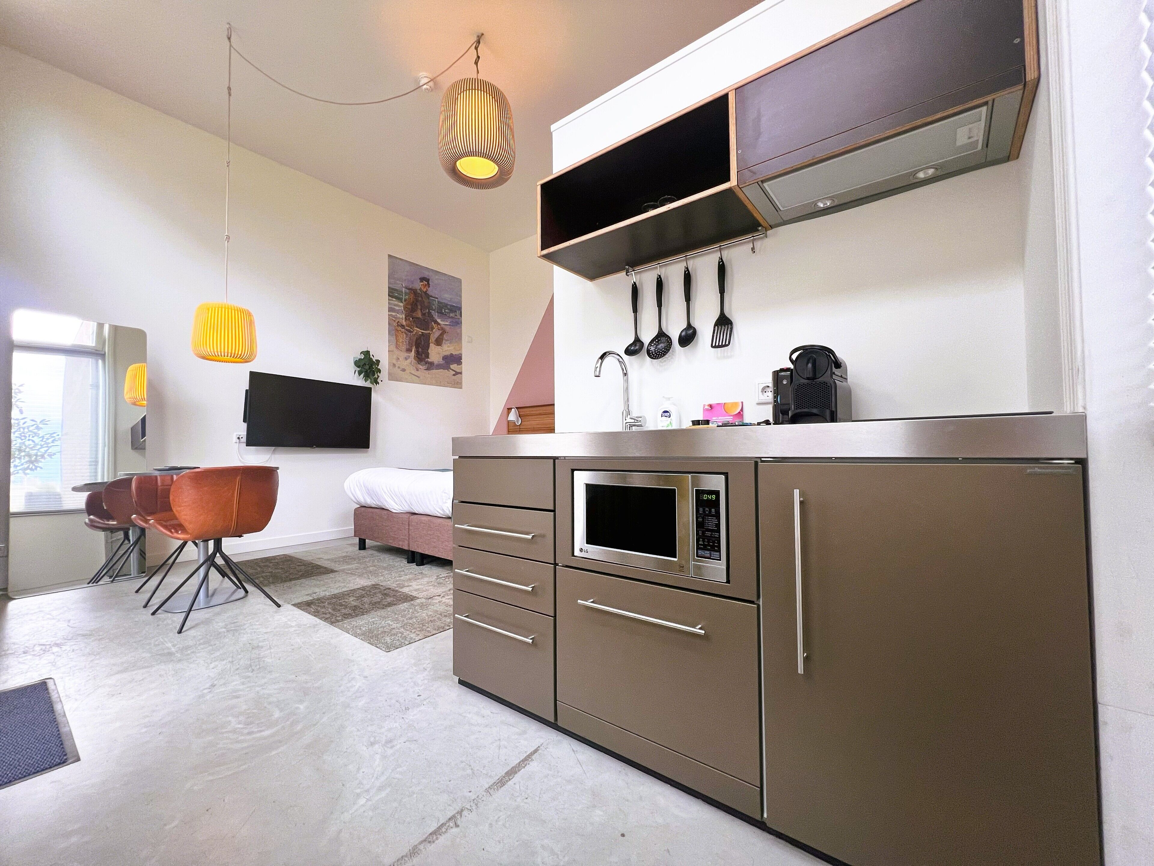 Una cocina moderna con electrodomésticos de acero inoxidable, un comedor con sofá y sillas, y un televisor de pantalla plana montado en la pared.