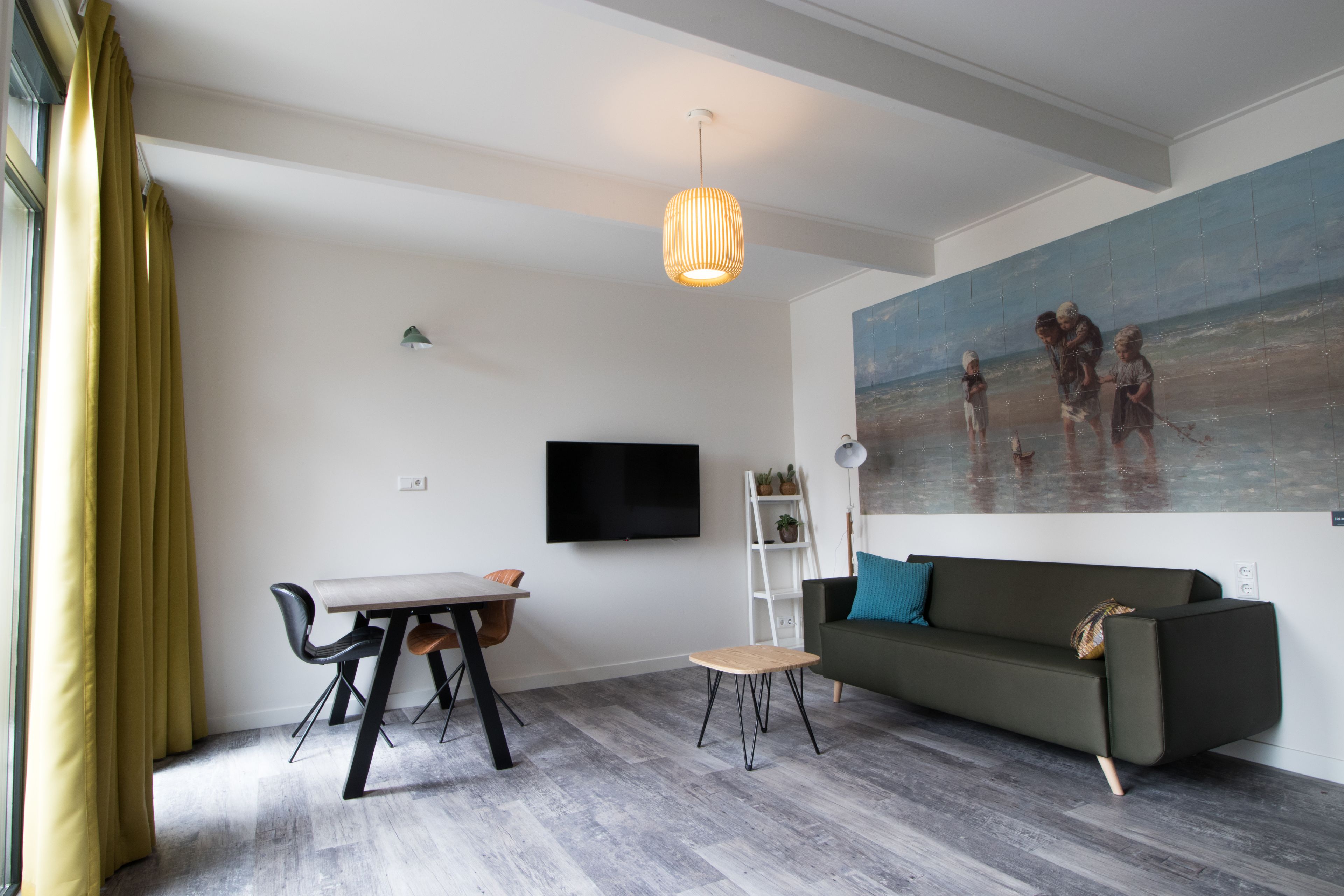 Una sala de estar moderna con comedor, un sofá, un cuadro con una escena de playa y un televisor en la pared.