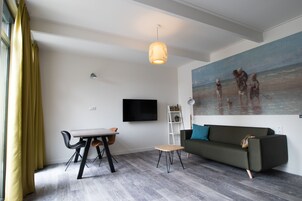 Una sala de estar moderna con comedor, un sofá, un cuadro con una escena de playa y un televisor en la pared.