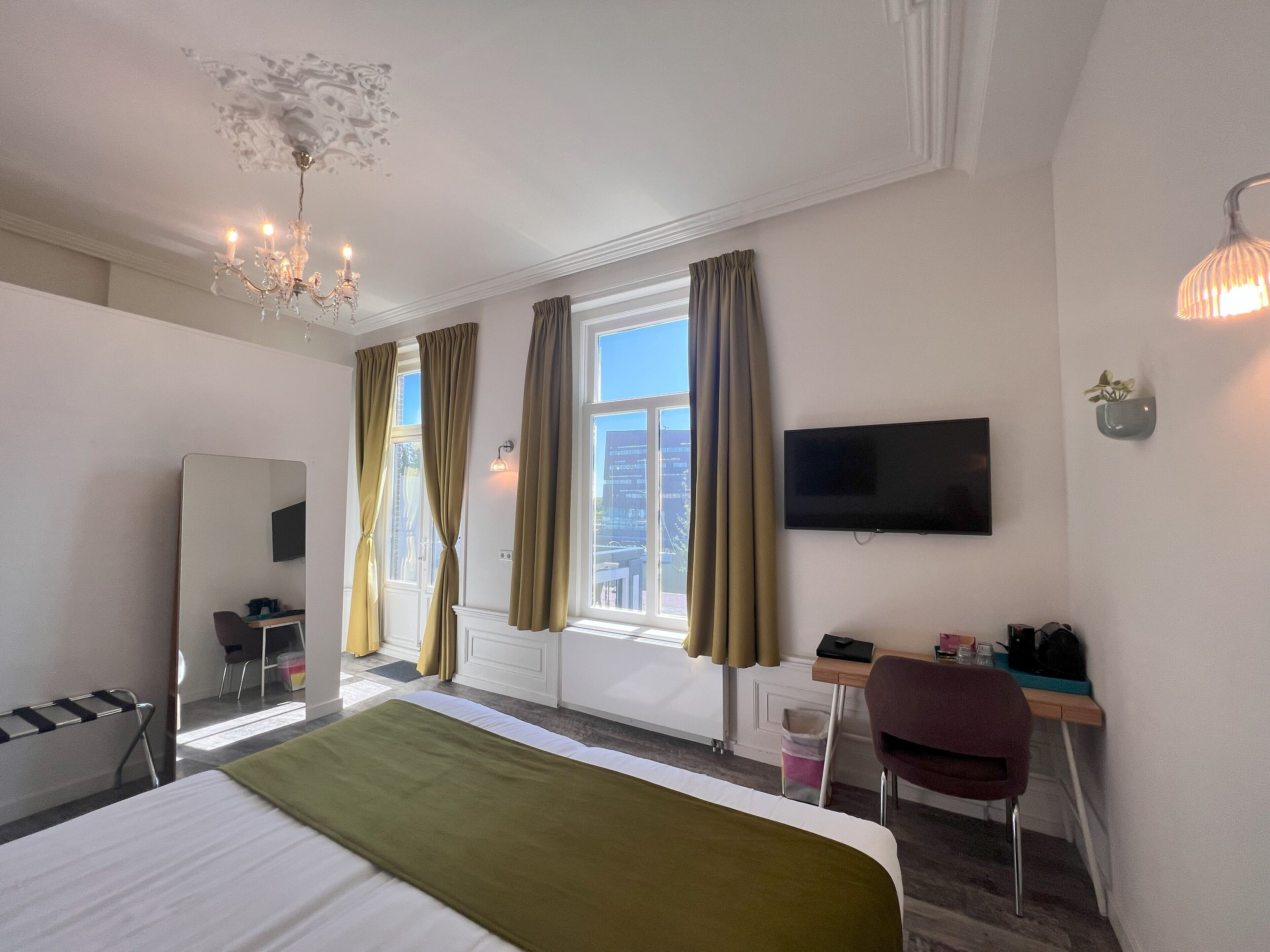 Une chambre d’hôtel avec un lit, un bureau, une chaise, une télévision et une fenêtre avec des rideaux.