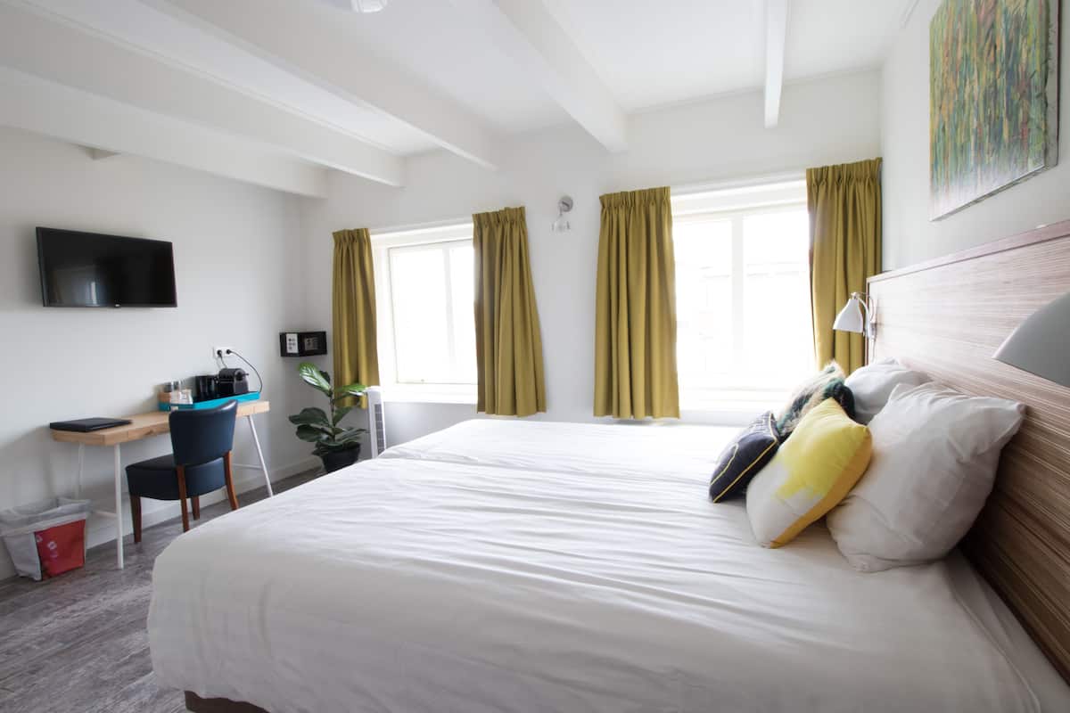 Quarto de hotel com uma cama grande, uma escrivaninha com cadeira, televisão e janela com cortinas.