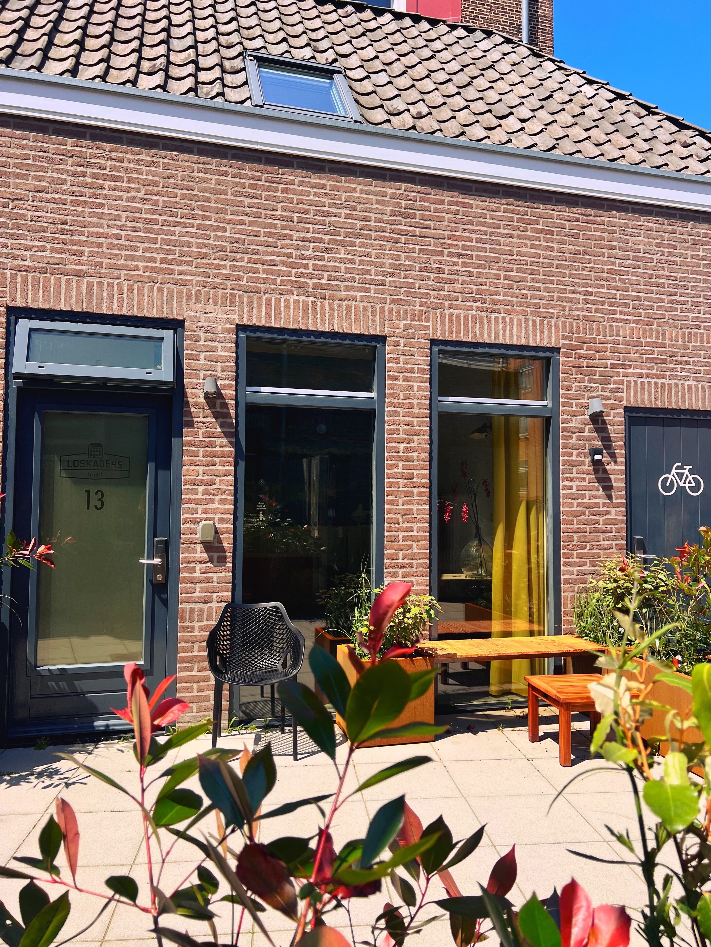 A brick building with a tiled roof, a door labeled "LOSKADE45", and a bicycle symbol indicating a bike-friendly area.