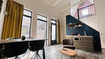 A modern kitchen with a dining area, large windows, and a staircase leading to an upper level.