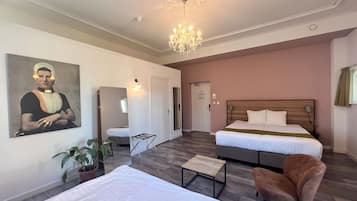 Une chambre d’hôtel avec deux lits, un lustre, un tableau, une plante en pot et un plancher en bois.