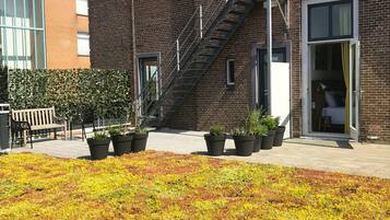 A brick building with a fire escape, potted plants, and a paved area with greenery.