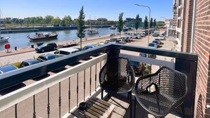 Un balcon donnant sur une rivière, des bateaux et des voitures garées.