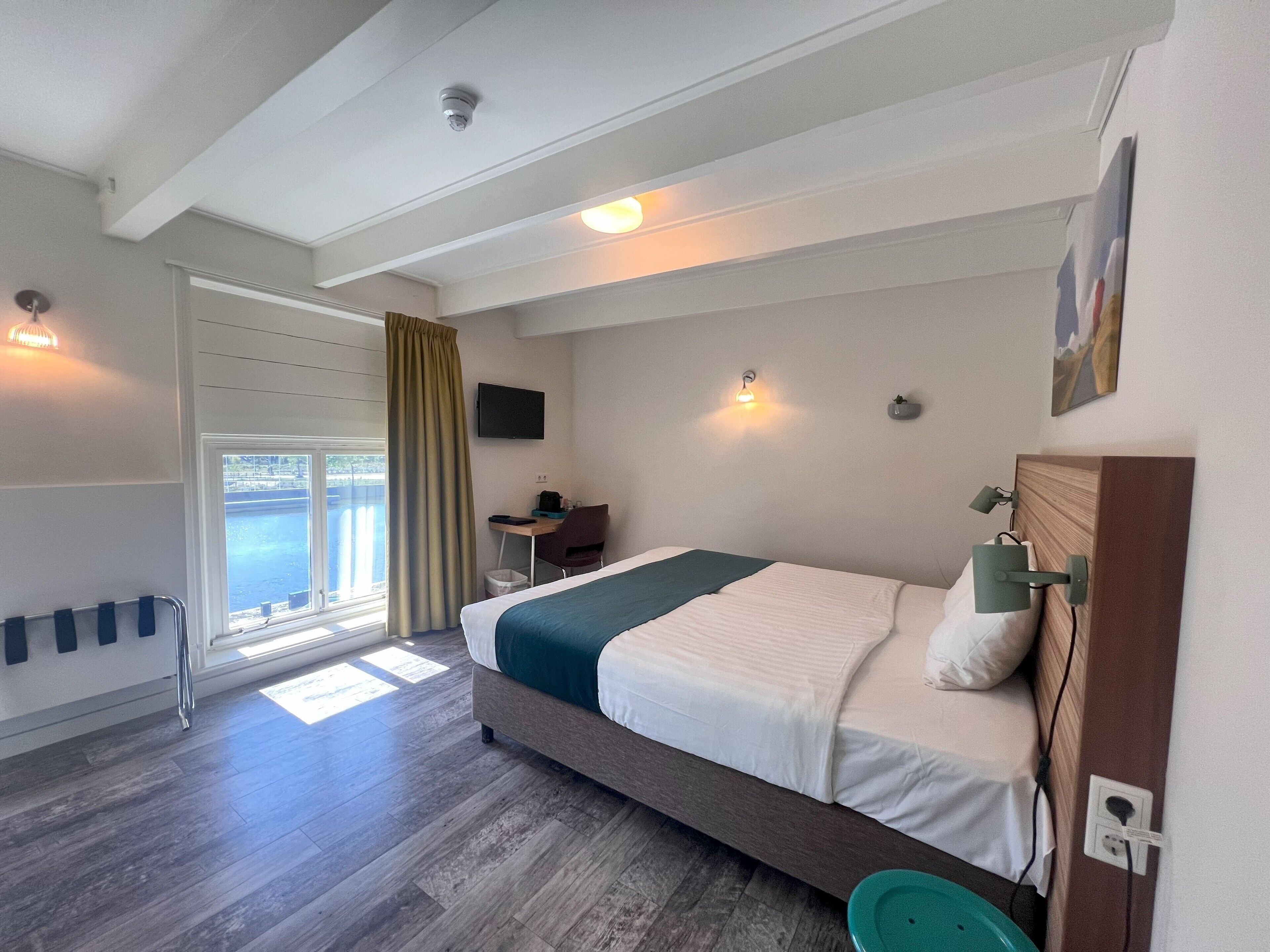 A hotel room with a bed, desk, chair, and a view of the water.