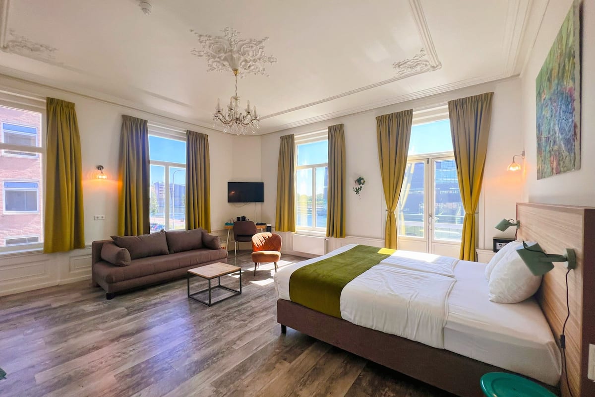 Quarto de hotel com uma cama grande, um sofá, uma mesinha e uma televisão.