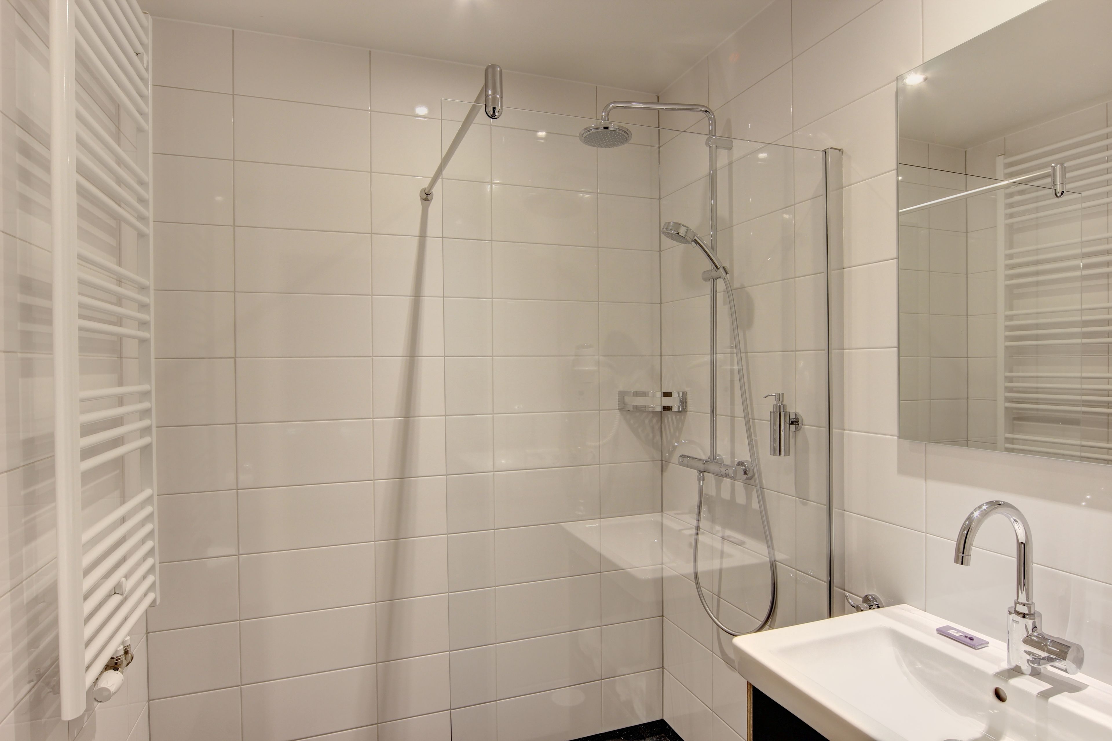 A modern bathroom with a glass-enclosed shower, a white sink, and a large mirror.