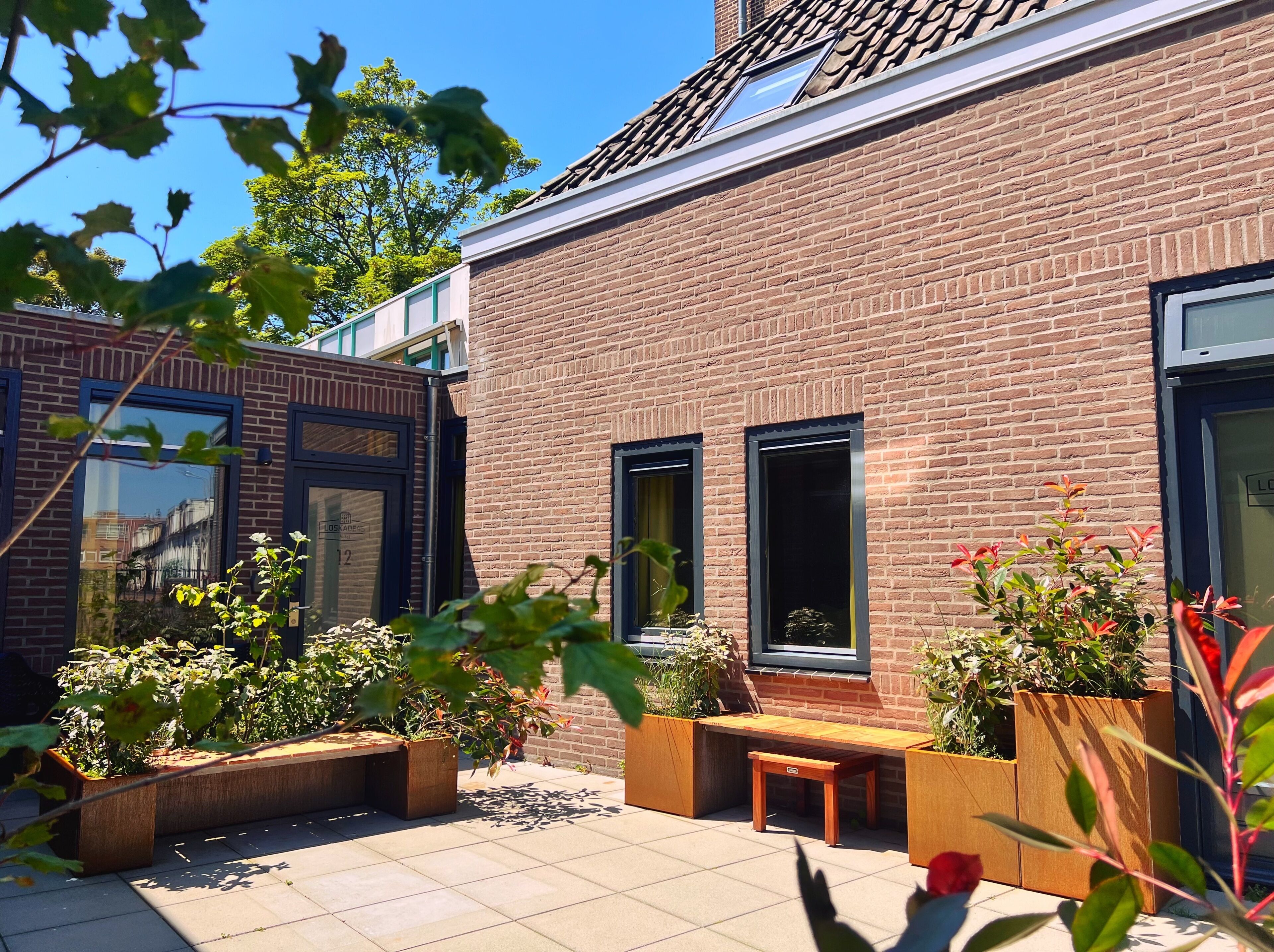 A brick building with large windows and a tiled patio area with wooden planters and benches.