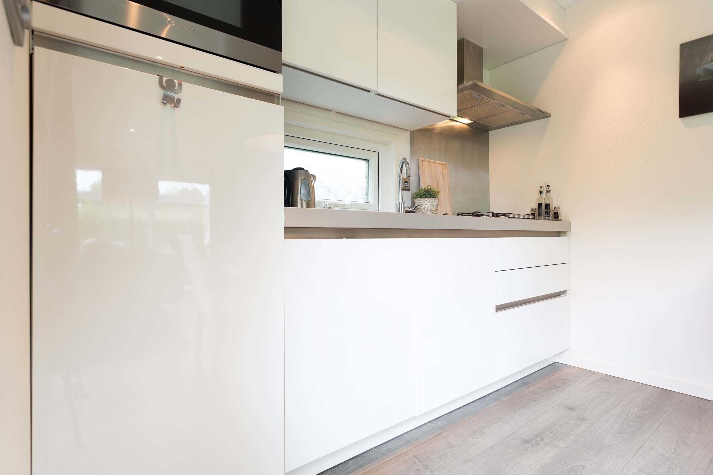 Une cuisine moderne avec des meubles blancs, une fenêtre et une hotte de cuisinière en acier inoxydable.