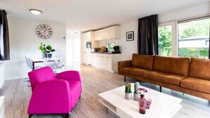 A modern living room with a bright ceiling, a large window, a sofa, a coffee table, and a dining area with a glass table and chairs. - TopParken Residence Lichtenvoorde (Lichtenvoorde)