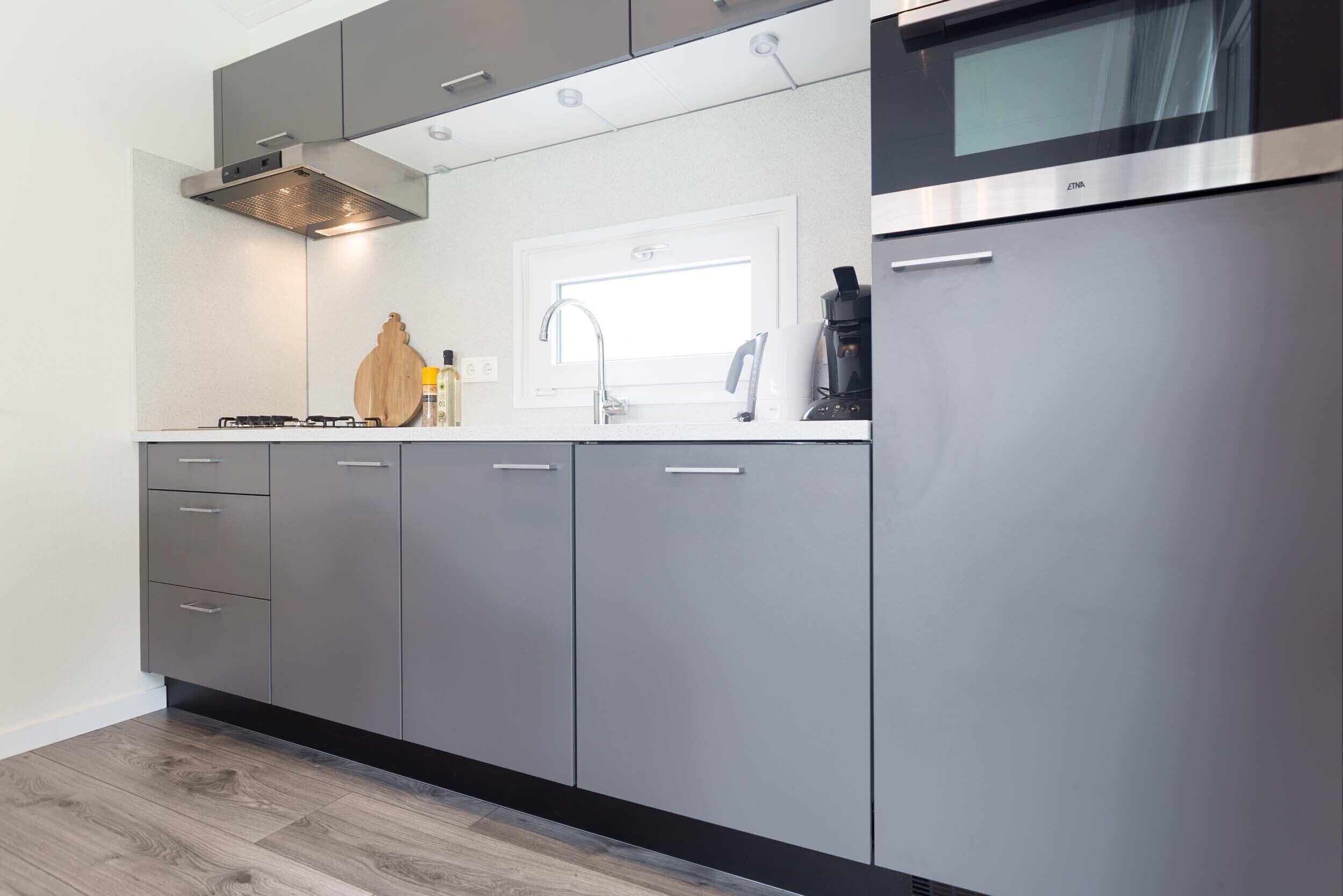 Une cuisine moderne avec des meubles gris, une hotte en acier inoxydable, un four à micro-ondes encastré et une fenêtre au-dessus de l’évier.