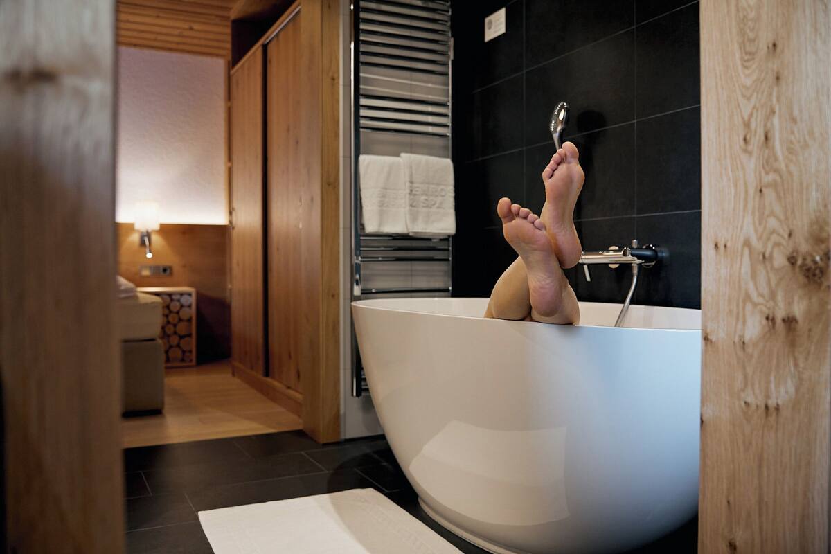 A modern bathroom with a freestanding bathtub, wooden flooring, and a towel rack with towels.