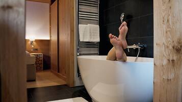 A modern bathroom with a freestanding bathtub, wooden flooring, and a towel rack with towels.