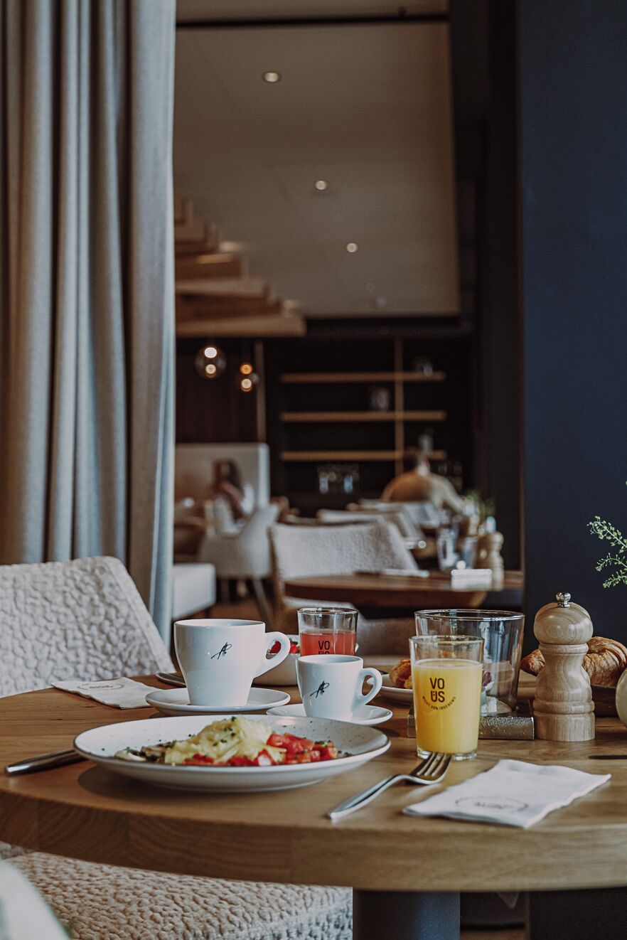 Une table à manger avec une assiette de nourriture, deux tasses, un verre de jus de fruits et un salier.