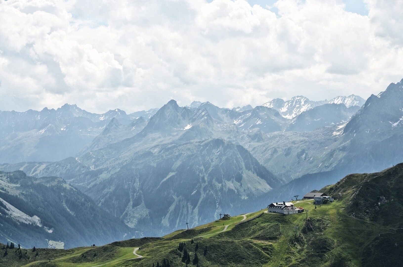 A mountain landscape with a building on a hill, surrounded by snow-capped peaks.