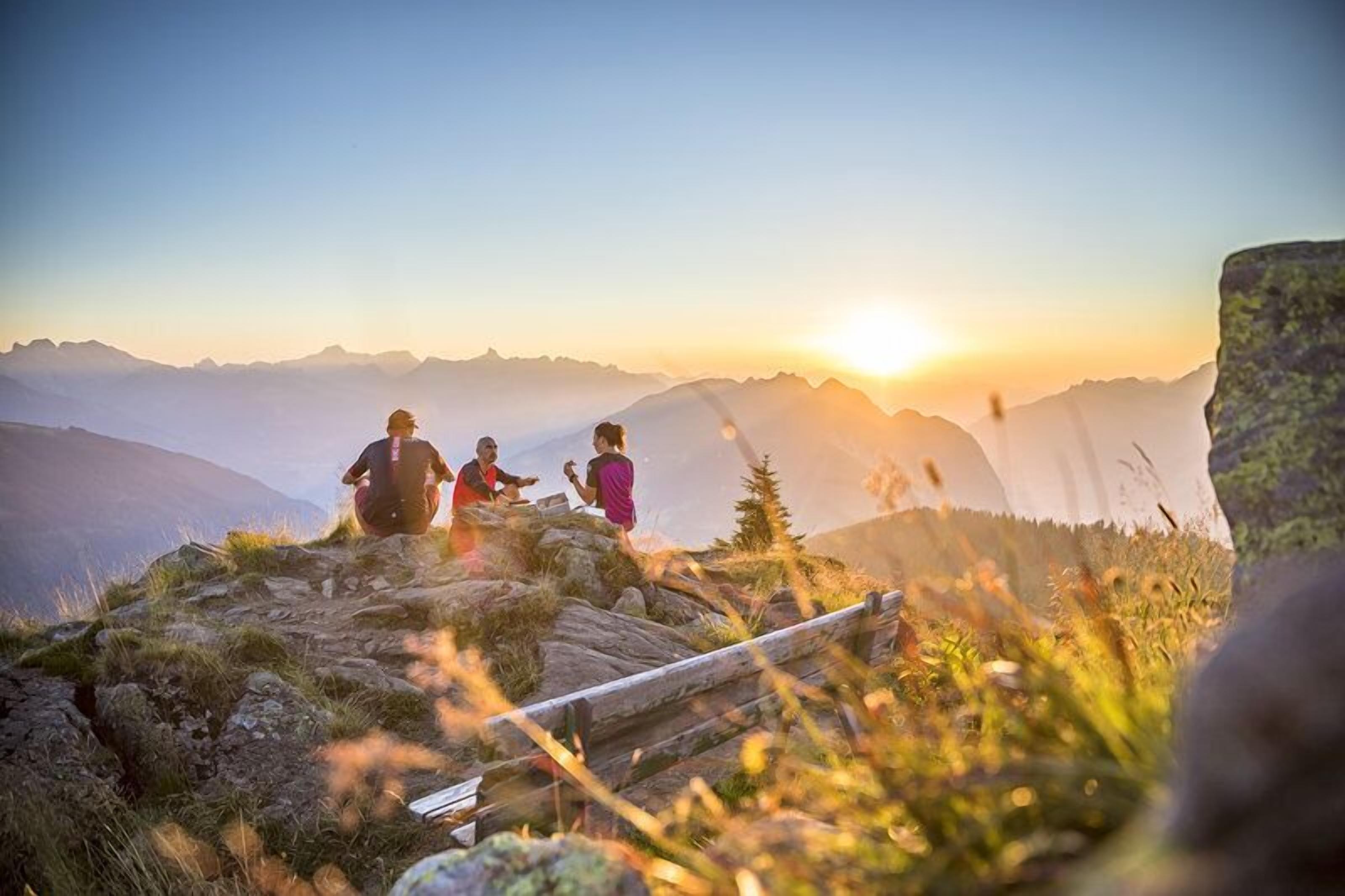 Een groep mensen op een bergpad, met een zonsondergang op de achtergrond.