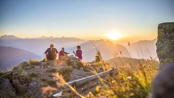 Een groep mensen op een bergpad, met een zonsondergang op de achtergrond.