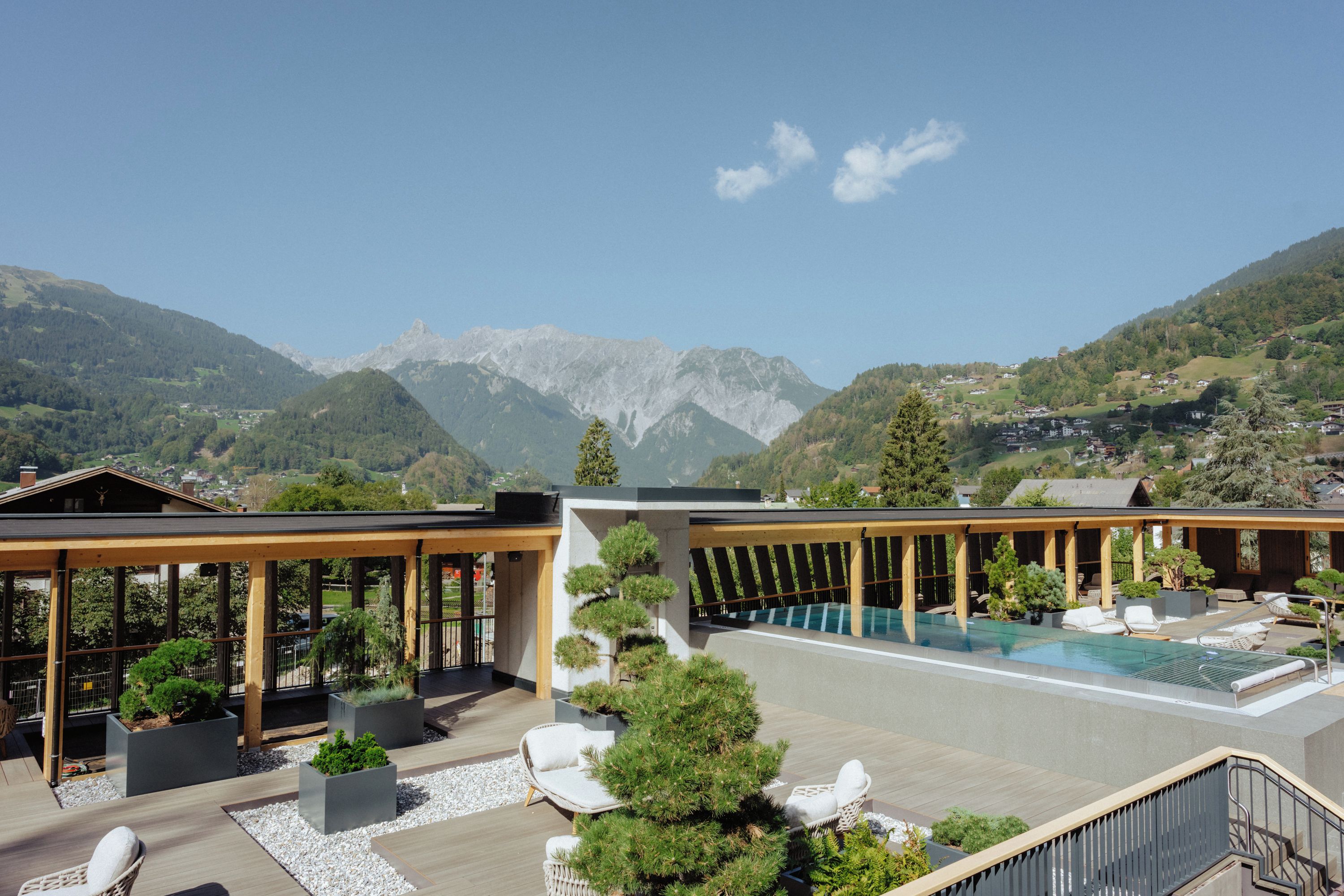 Área moderna de piscina ao ar livre com vista para montanhas, pérgulas de madeira e espreguiçadeiras.