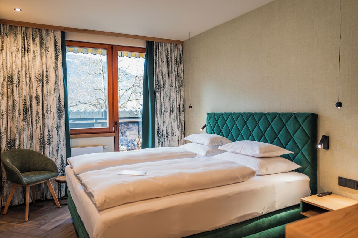 A hotel room with a large bed, a chair, a nightstand, and a window with curtains.