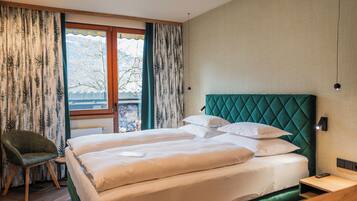 A hotel room with a large bed, a chair, a nightstand, and a window with curtains.