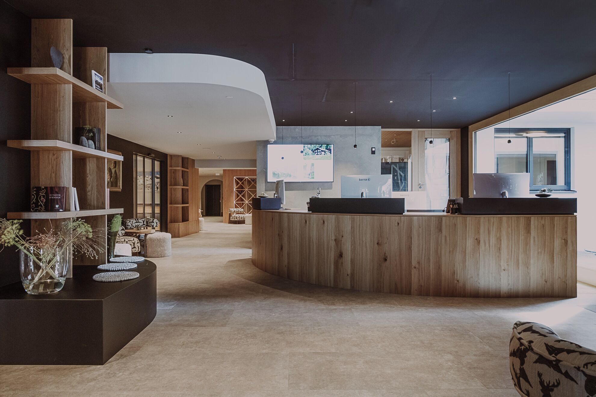 A modern reception area with a curved wooden counter, a seating area with patterned cushions, and a large window providing natural light.