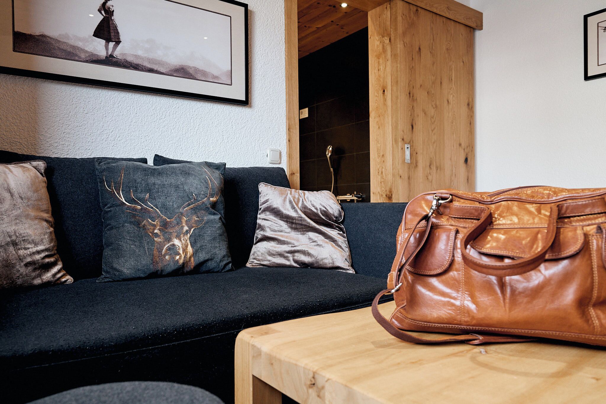A modern living room with a dark sofa, a wooden table, and a brown leather bag.