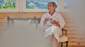 A person sitting on a bench in a room with large windows, holding a glass. - Alpenrose Aktiv & Spa (Schruns)