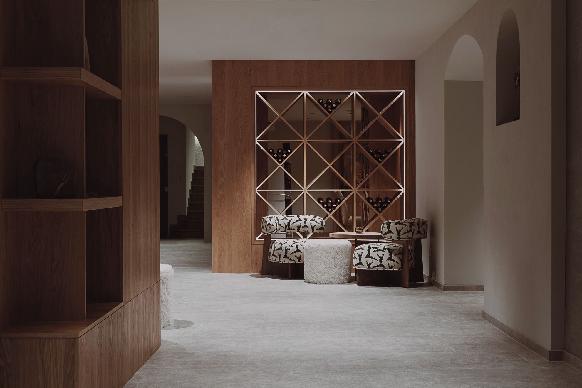 A hallway with a wooden bookshelf, a patterned seating area, and a geometric wall design.