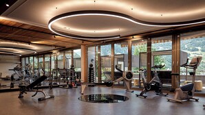 A modern gym with various exercise equipment, large windows, and a view of a mountainous landscape. - Alpenrose Aktiv & Spa (Schruns)