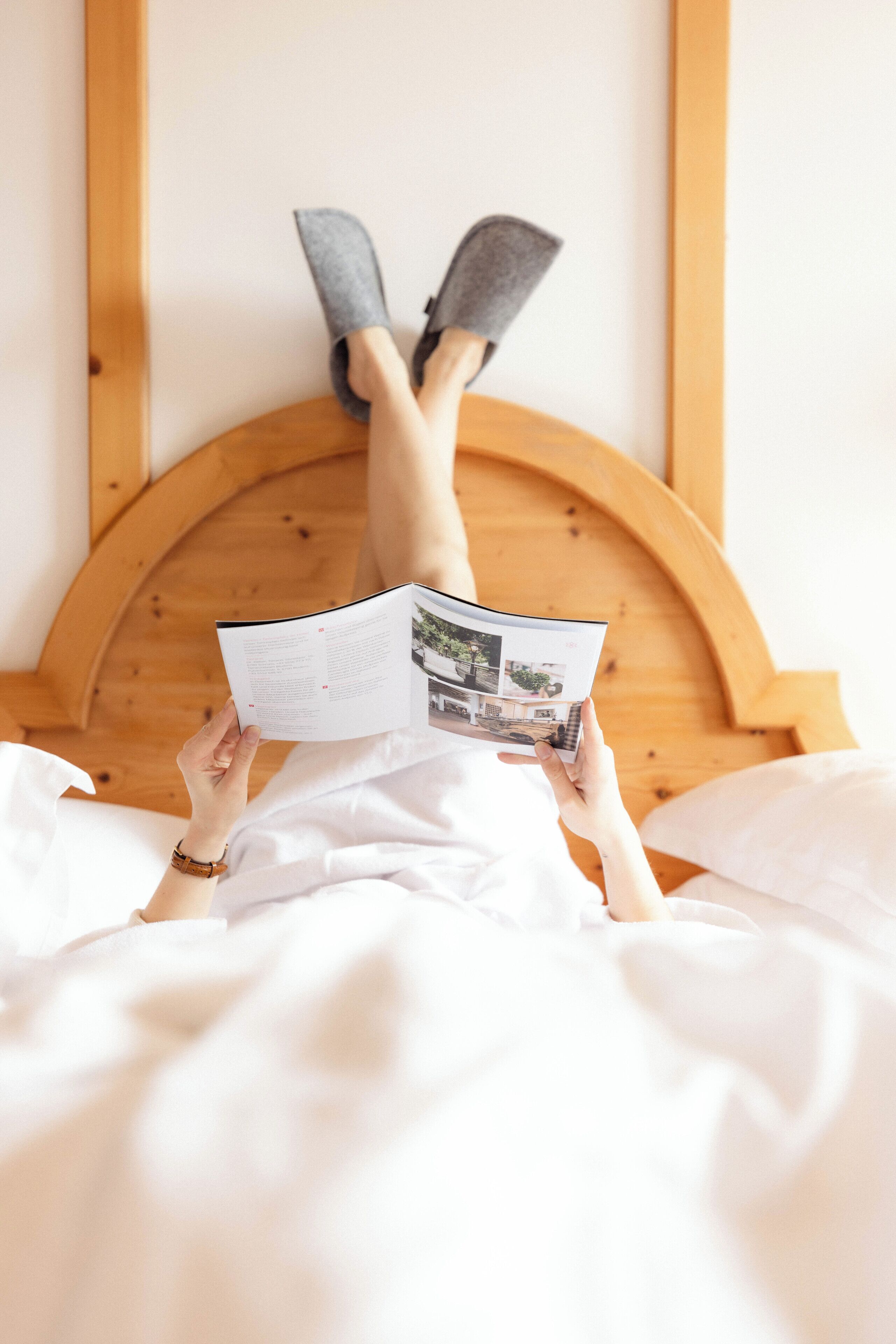 Eine Person liegt im Bett und liest eine Zeitschrift.