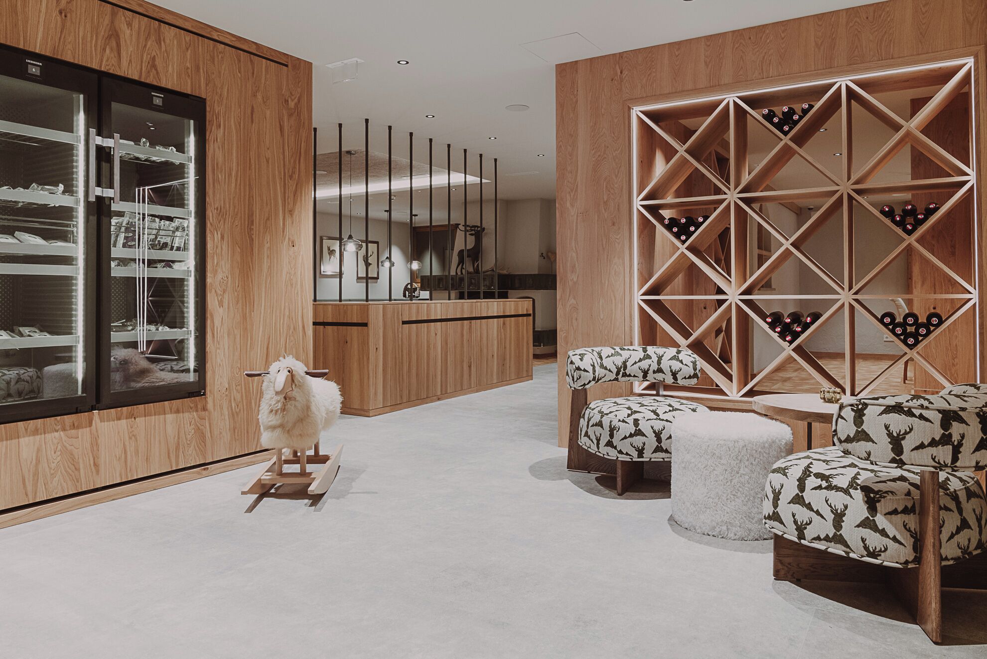 A modern interior with a wooden shelving unit displaying wine bottles, a plush sofa with a patterned cover, and a decorative sheep sculpture.