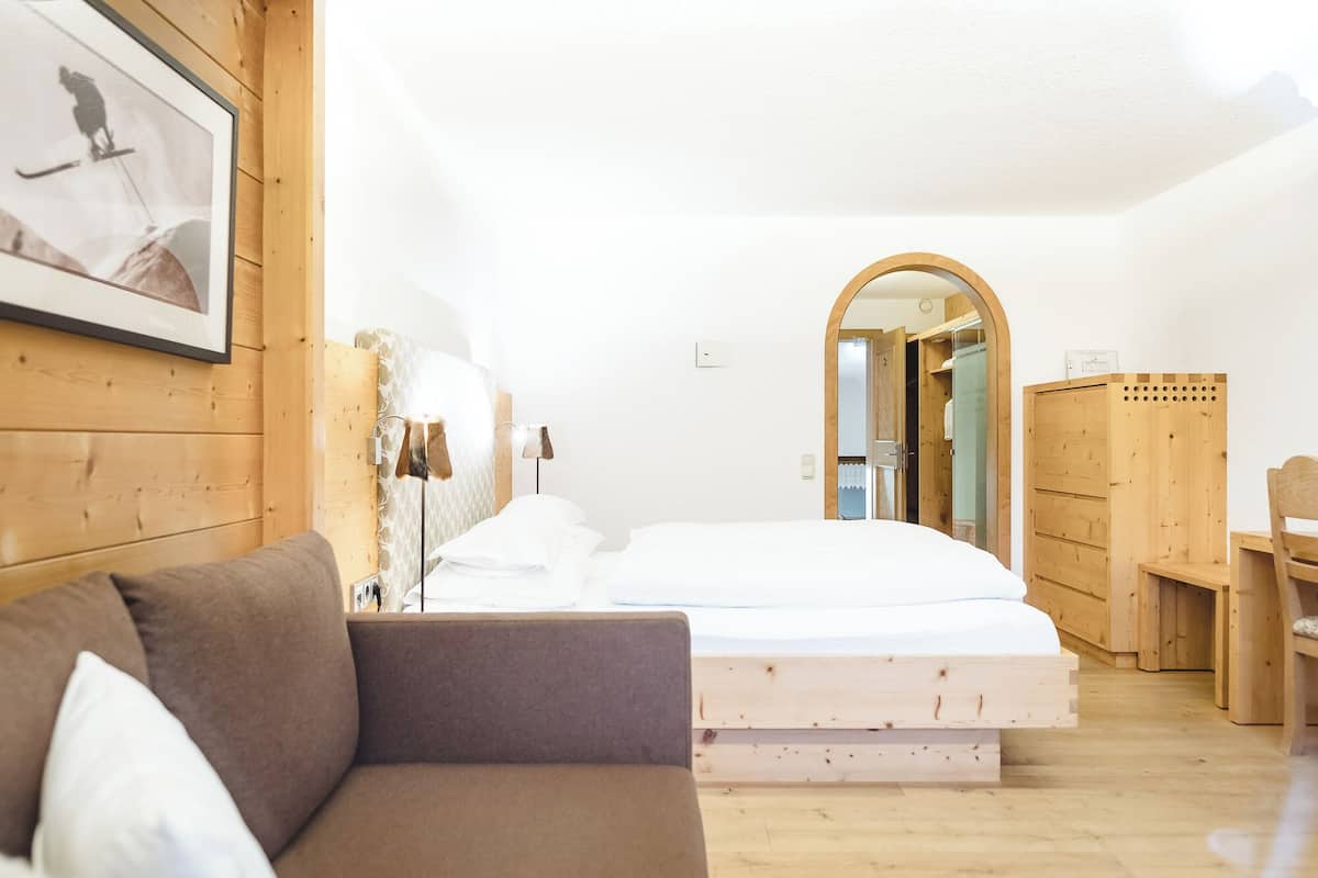 A room with a bed, a wooden wardrobe, a framed picture on the wall, and a wooden floor.
