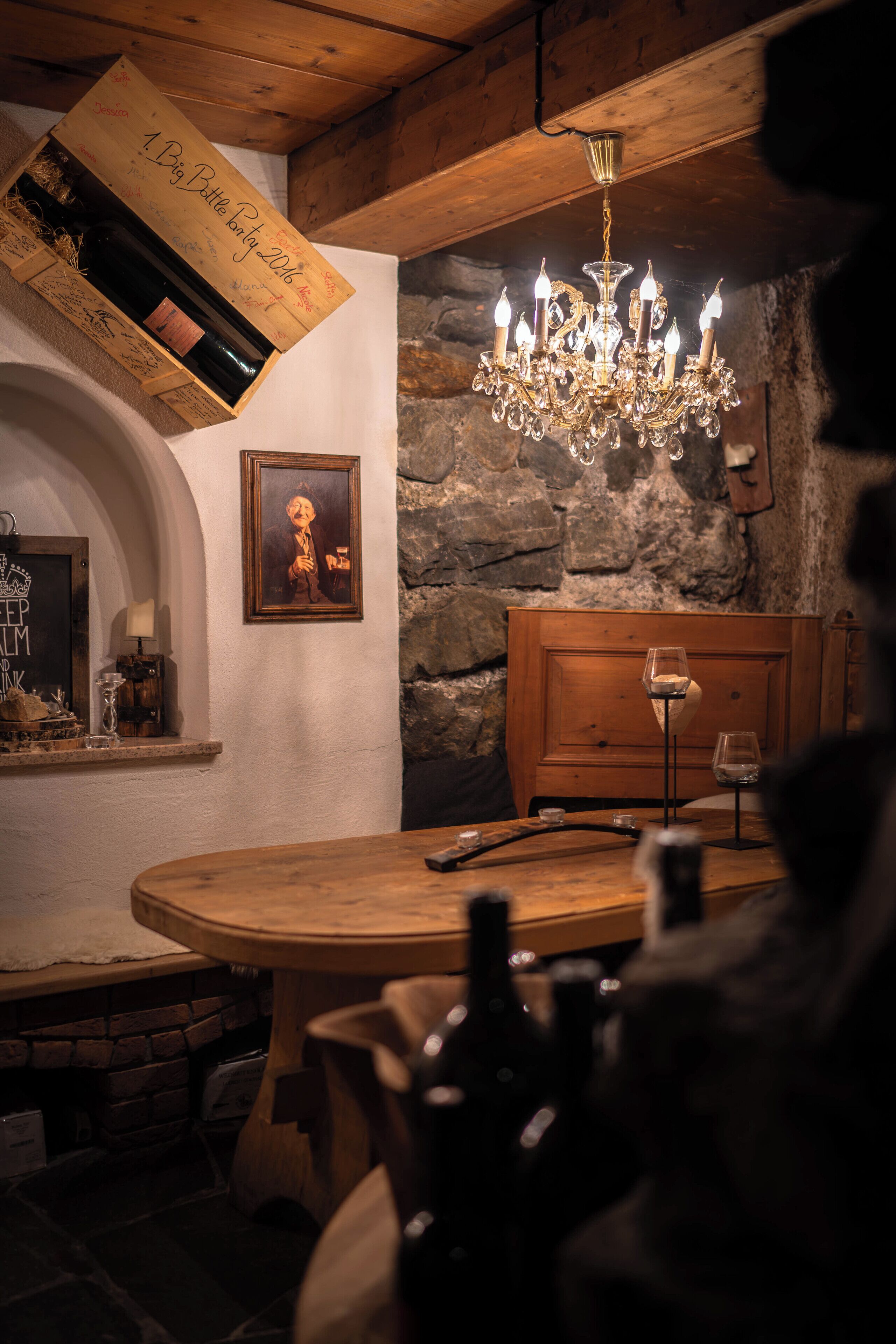 A rustic dining area with a wooden table, a chandelier, and a wine rack with bottles.