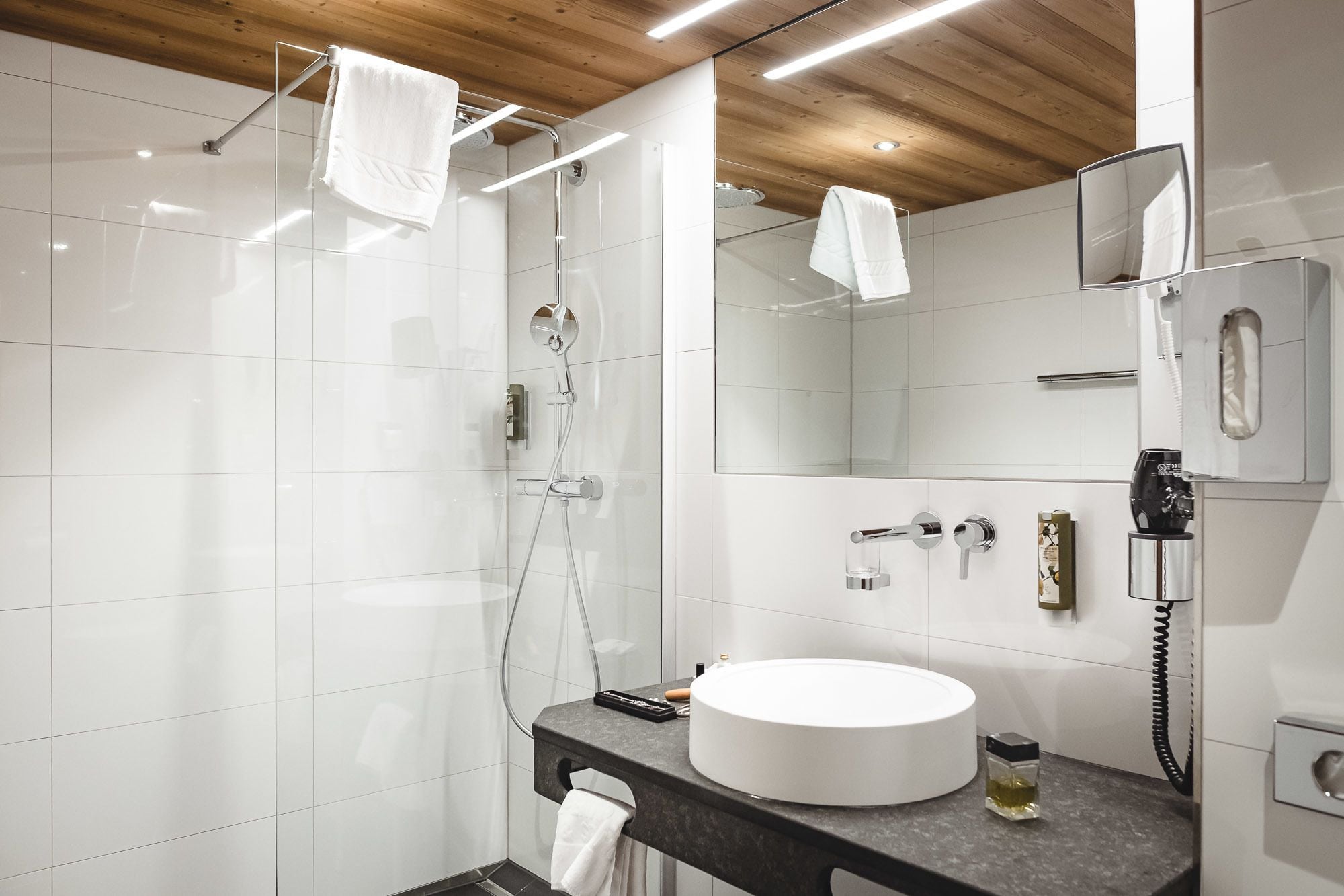 A modern bathroom with a glass-enclosed shower, a round white sink, and a large mirror.