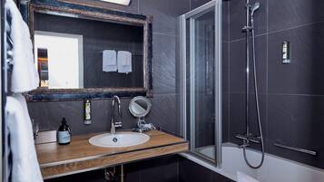 Une salle de bain moderne avec un meuble-lavabo en bois, un grand miroir, une douche à parois de verre et des murs recouverts de carreaux foncés.