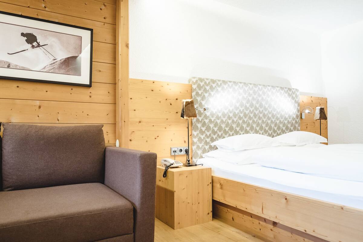 A wooden room with a bed, a nightstand, a lamp, a framed picture, and a sofa.