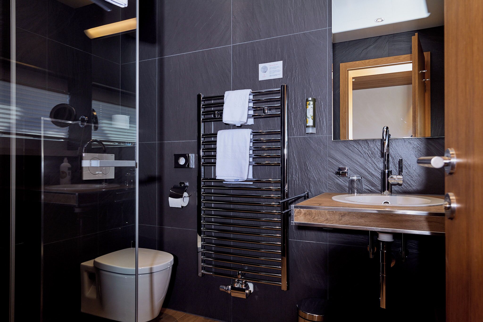 A modern bathroom with a glass shower enclosure, a toilet, a towel rack with two towels, a sink with a mirror, and a wooden-framed mirror above the sink.