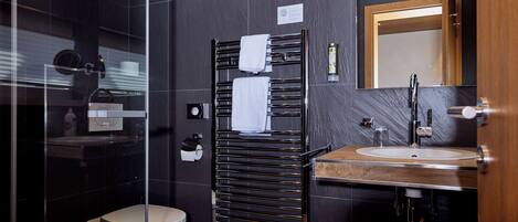 A modern bathroom with a glass shower enclosure, a toilet, a towel rack with two towels, a sink with a mirror, and a wooden-framed mirror above the sink.