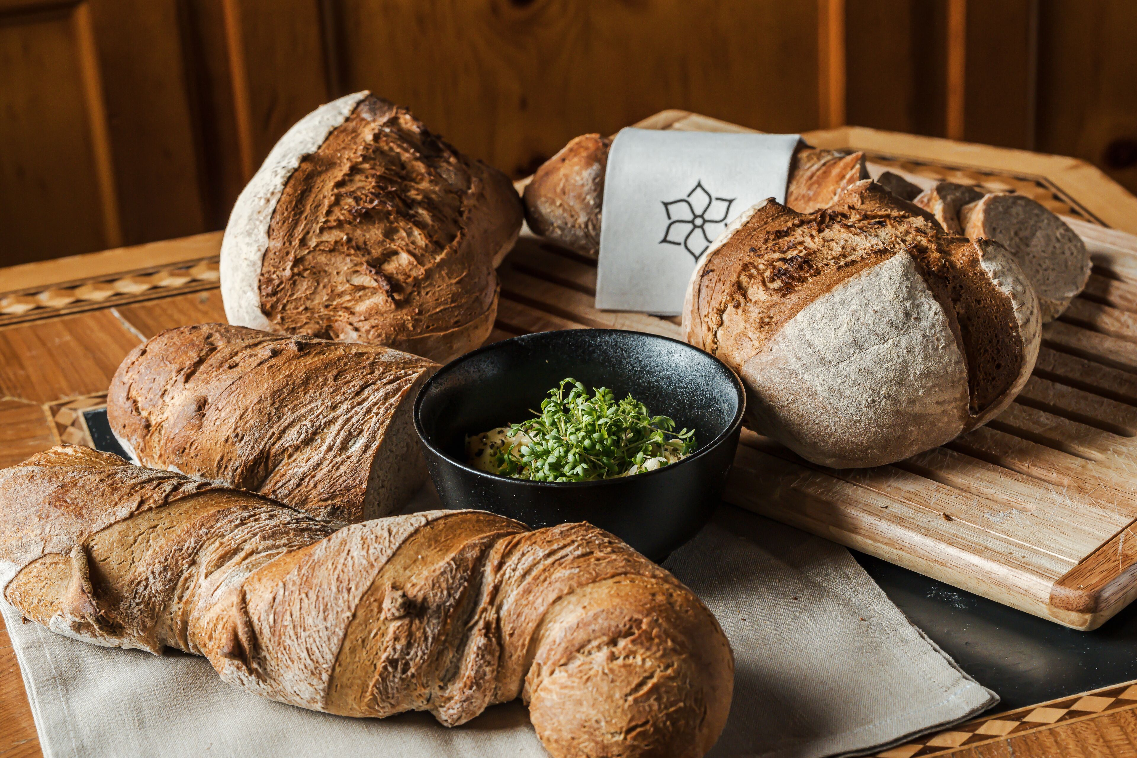 A variety of breads and a bowl of greens on a wooden table.