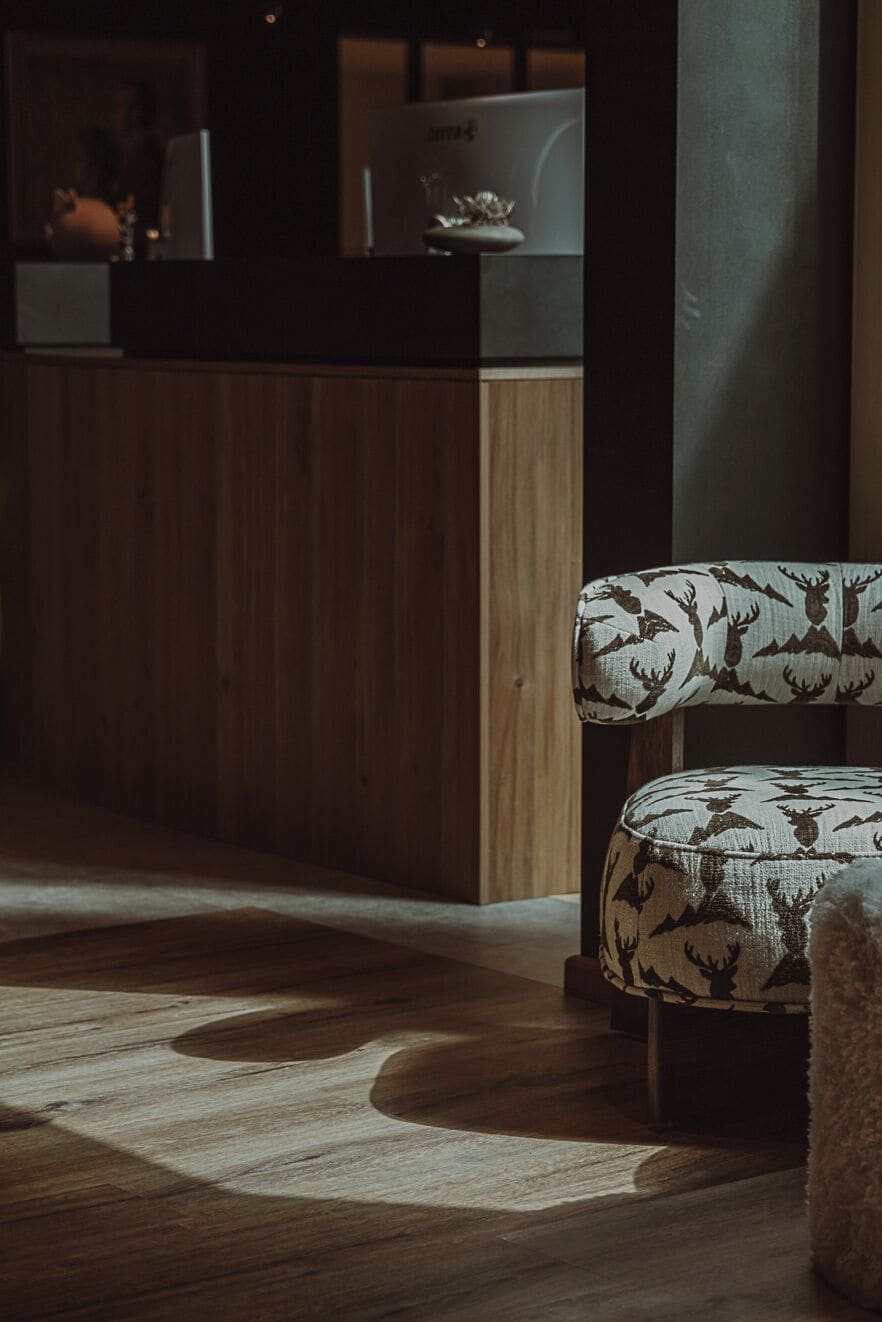 Suelo de madera con un tapete estampado, una silla con tapicería de estampado de ciervo, y una zona de cocina con un refrigerador y un fregadero.