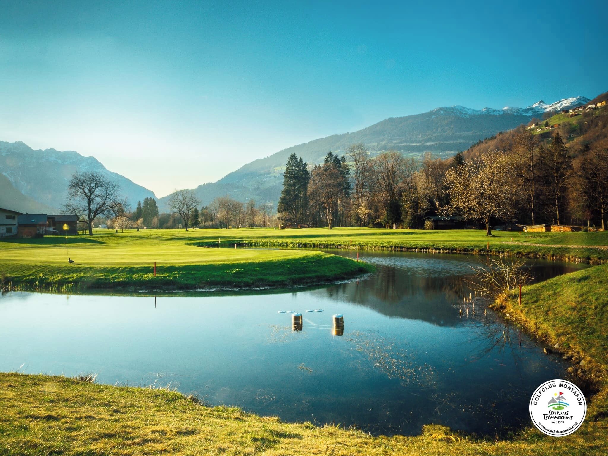 A golf course with a pond, trees, and mountains in the background.