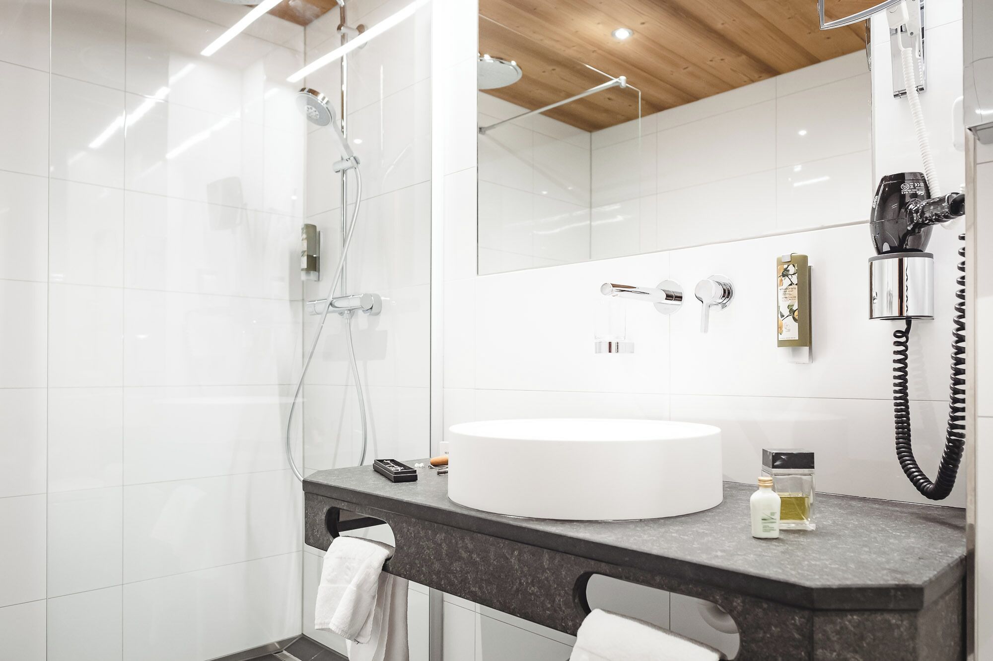 Une salle de bain moderne avec un lavabo rond, un miroir, un sèche-cheveux et un porte-serviettes.