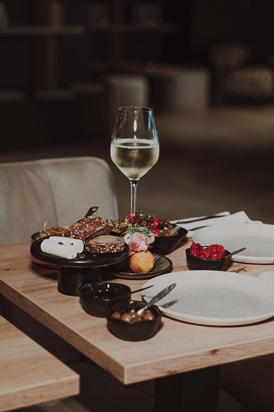 Una mesa de comedor con diferentes platos, una copa de vino blanco y un bol de bayas.