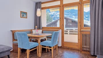 A cozy dining area with a wooden table and blue upholstered chairs, a small painting on the wall, and a view of snowy mountains through large windows.