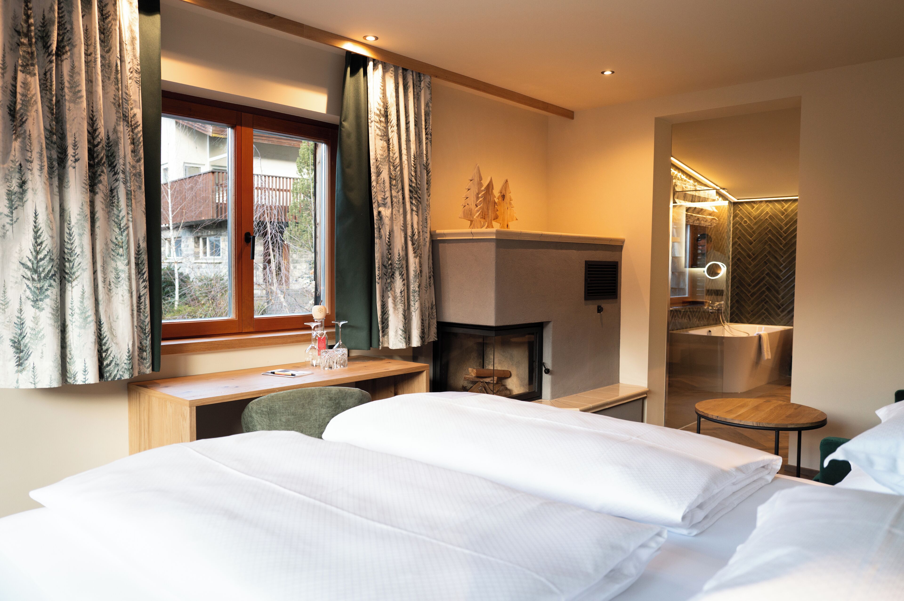 A hotel room with a bed, desk, chair, fireplace, and a small bathroom with a bathtub.