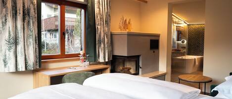 A hotel room with a bed, desk, chair, fireplace, and a small bathroom with a bathtub.
